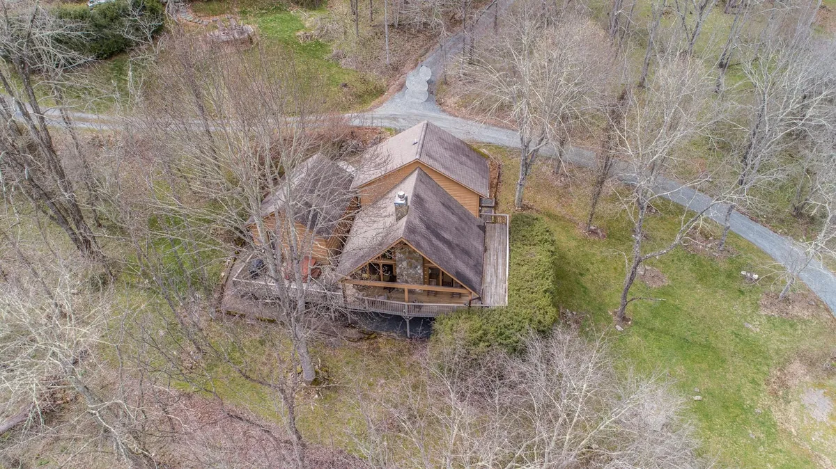 An inviting view of the wooden cabin nestled among mature trees with a visible pathway leading toward the entrance. The natural surroundings evoke a sense of peace and outdoor adventure, ideal for families looking to explore nature together. Seasonal touches suggest year-round appeal, from fall foliage to winter snow activities.