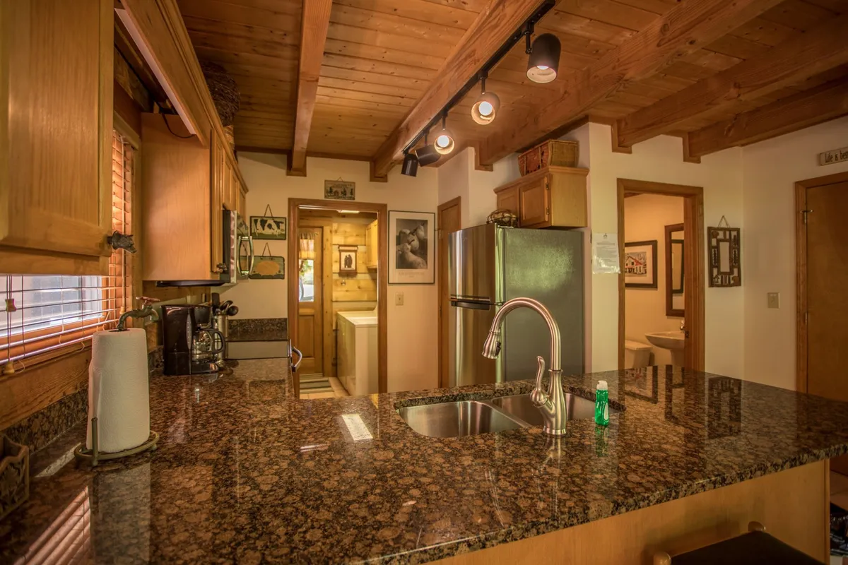 A welcoming kitchen with granite countertops, stainless steel appliances, and timber beams overhead. The space is designed for gatherings, with ample room for both cooking and socializing, hinting at the hustle and bustle of group or family stays—including four-legged family members.