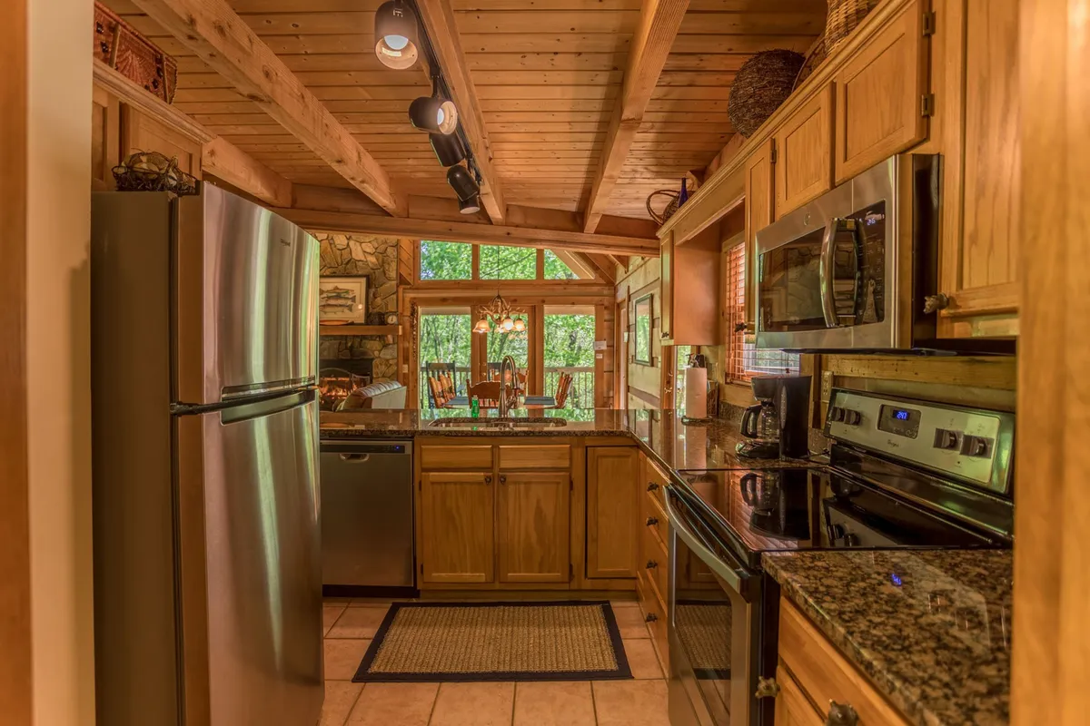 A well-equipped kitchen with stainless steel appliances, granite countertops, and wooden cabinetry. Large windows provide a view of the outdoors, and the space is perfectly suited for group cooking and socializing.