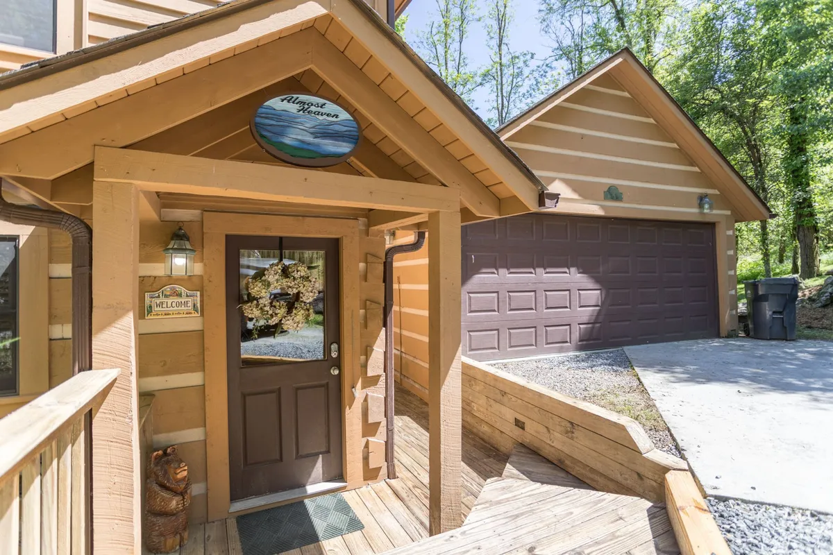 A welcoming front door adorned with a wreath and a 'welcome' sign opens onto a wooden deck, suggesting arrival and access to outdoor spaces. The deck area hints at opportunities to gather and enjoy the surrounding environment, seamlessly blending the property with its natural setting.