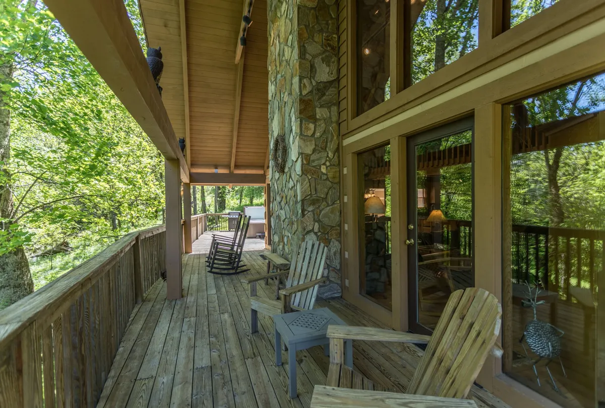 A spacious wooden deck featuring classic rocking chairs and surrounded by lush greenery. The large windows and tranquil setting suggest a seamless indoor-outdoor experience, perfect for relaxing with family after a day of exploring or enjoying meals outdoors. The deck provides a welcoming space for social gatherings or quiet moments in nature.
