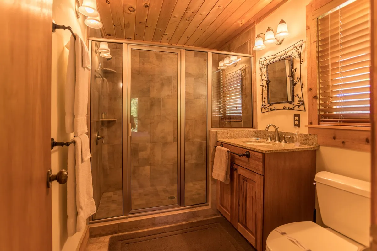A luxurious walk-in tiled shower complemented by wooden cabinetry and a decorative framed mirror, exuding a spa-like ambiance perfect for unwinding after a day of adventure.