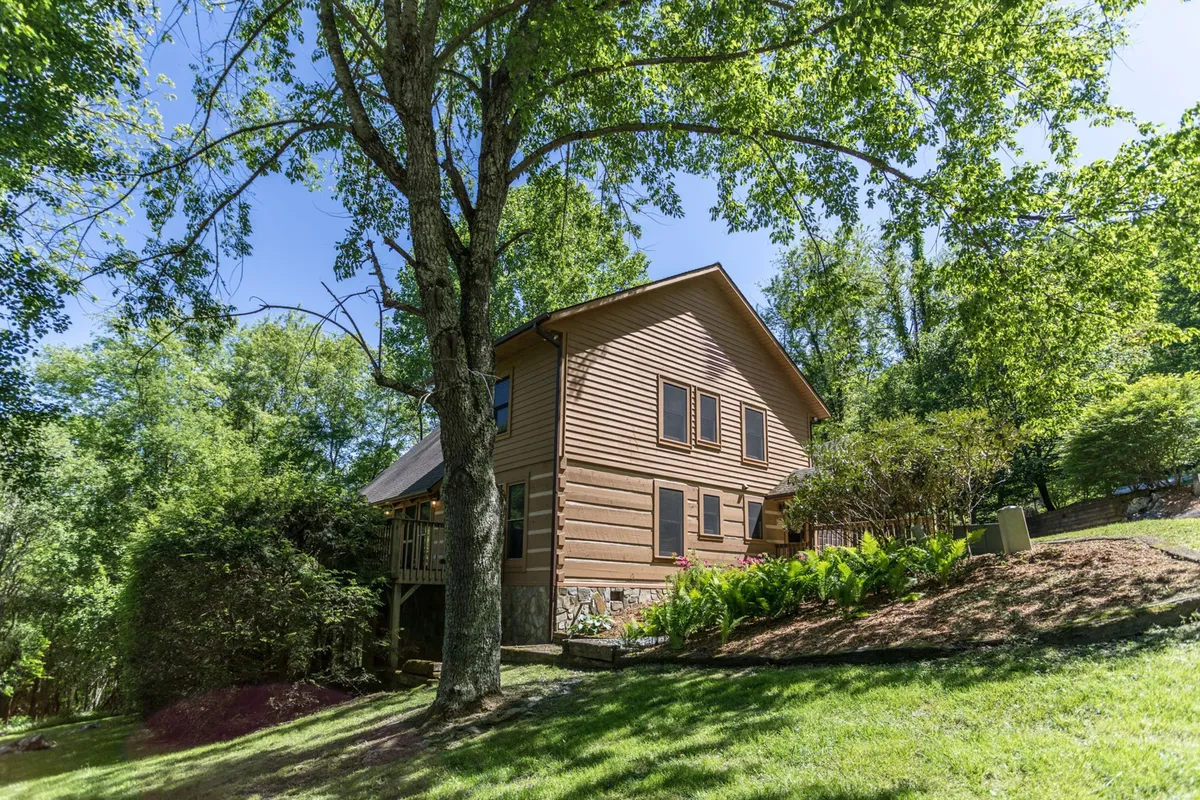 An exterior view of the house with a large yard framed by a prominent tree and landscaped garden. The open space and surrounding nature invite families and pets to play, relax, and explore the outdoors together.